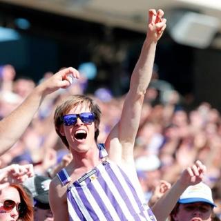 A happy, 在一场拥挤的足球比赛中，一名身穿条纹工作服、戴着紫色太阳镜的欢呼学生做出了两个手指的“青蛙加油”手势.